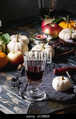 Autumn holiday table decoration setting with decorative pumpkins, apples, red leaves, glasses of red wine, candle over wooden table. Rustic style Stock Photo
