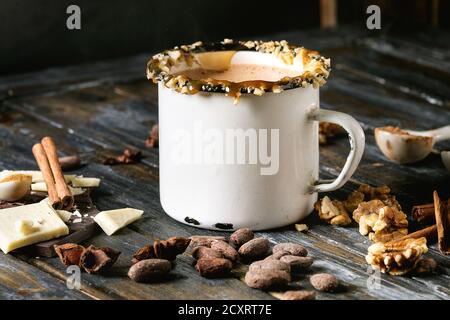 Vintage mug of hot chocolate, decor with nuts, caramel, spices. Ingredients above. Chopped dark and white chocolate, cocoa beans, anise over old woode Stock Photo