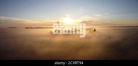 Morning fog, sunbeams and long shadows in the fog that stretched between the trees in the valley near the village. Stock Photo