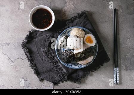 Blue plate with different size rice balls with black sesame and seaweed nori, served with soft boiled eggs, soy sauce, chopsticks over gray table. Asi Stock Photo