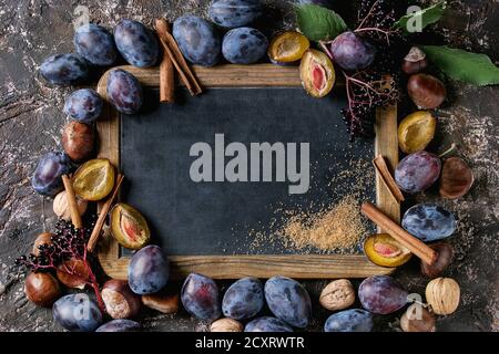 Autumn frame from plums, nuts, cinnamon and brown sugar with empty vintage chalkboard over brown concrete background. Top view with space for text. Fa Stock Photo