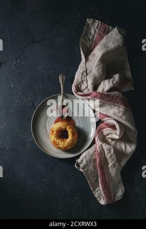 Homemade donut with jam on gray plate with vintage spoon and textile towel over dark texture background. Top view with space Stock Photo