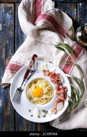 Italian traditional pasta alla carbonara with yolk, pancetta bacon, parmesan cheese, thyme, served in white plate on textile linen over old wooden pla Stock Photo
