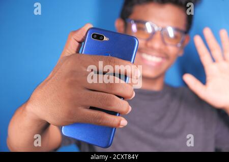 Smiling young man in glasses is using his phone to make a video call Stock Photo