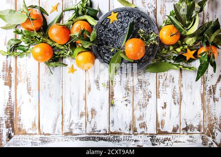 Christmas table decorations with clementines or tangerines with leaves and green branches on black ornate board over white wooden plank table. Top vie Stock Photo