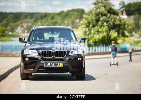 GRODNO, BELARUS - JUNE 2020: BMW X3 II F25 2.0i xDrive selective focus front view with boys passing by on hoverboards outdoors on sunny road summer Stock Photo