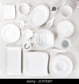Big set of empty white porcelain plates and other tableware different size and shapes over white linen tablecloth. Flat lay Stock Photo