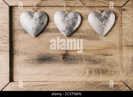 Love Valentines day greeting card with three silver hearts on rope cord over wooden texture background. Top view, copy space Stock Photo