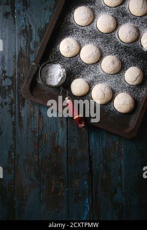 Homemade almond cookies with sugar powder, with vintage sieve, on old oven tray over dark blue wooden table. Dark rustic style. Top view, space Stock Photo