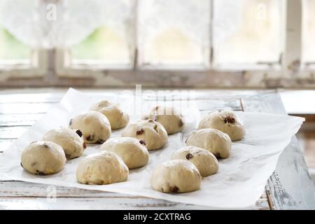 Raw unbaked buns. Ready to bake homemade Easter traditional hot cross buns on baking paper over white wooden table with window at background. Natural Stock Photo