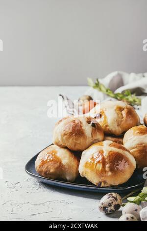 Homemade Easter traditional hot cross buns on blue plate with textile and colored quail eggs over white texture background. Copy space. Toned image Stock Photo