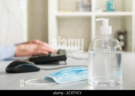 Antibacterial gel dispenser with surgical mask on office desk Stock Photo
