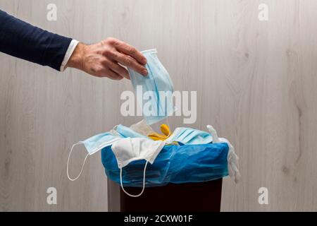 Man's hand throwing used surgical mask in the garbage. Stock Photo