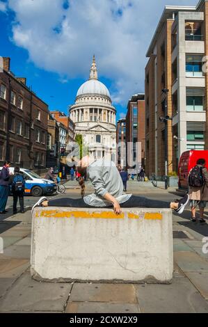 London, United Kingdom - September 18, 2017: Girl doing gymnastic splits pose on the stone in downtown of London full of walking people with Saint Pau Stock Photo