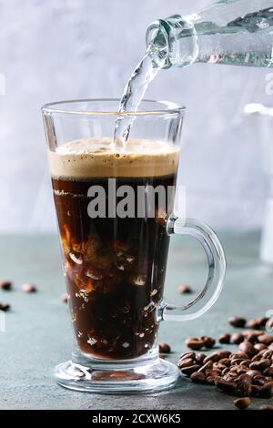 Fizzy iced Coffee espresso with pouring sparkling water from bottle and roasted beans around over grey green texture table. Modern drink. Stock Photo