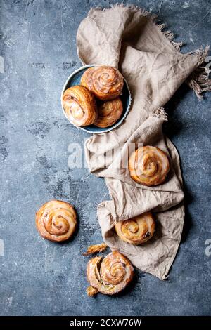 Homemade glazed puff pastry cinnamon rolls with custard and raisins on textile linen over blue texture background. Top view, space Stock Photo