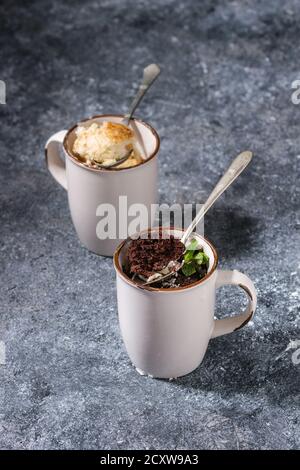 Chocolate and vanilla caramel mug cakes from microwave with spoons over blue kitchen table. Stock Photo