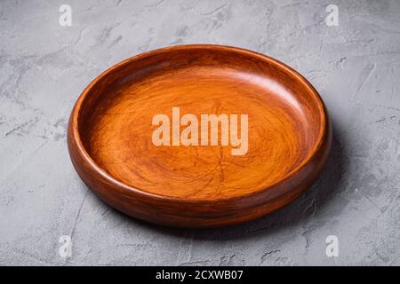 Empty round handcrafted brown wooden plate on stone concrete background, angle view Stock Photo