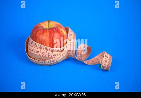 One apple a day for your health. Red apple with centimeter tape on a blue background. Stock Photo