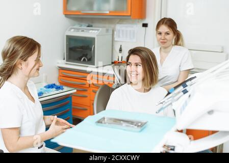 Medical dentist team talking with patient woman talking at dental clinic office preparing for treatment. Female dentist and her assistant in dental office talking with female patient. Stock Photo