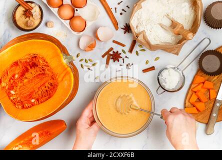Woman prepares pumpkin dough for homemade pancakes, muffins, pies or waffles. Ingredients on the marble table - flour, eggs, sugar, cinnamon, cardamom Stock Photo