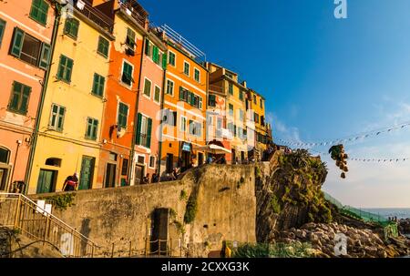 Nice panoramic view of the historic colourful tower houses in a row at the wharf and a gilded bunch of grapes hanging in the centre of Riomaggiore in... Stock Photo