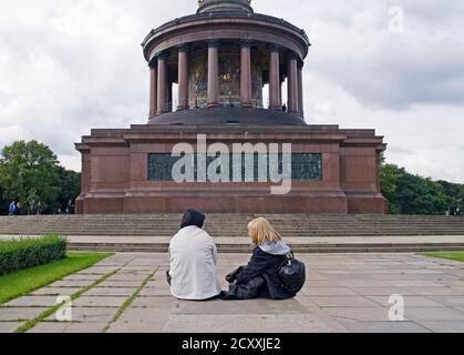 young couple of tourists sitting in front of Siegessaule monument,  Tiergarten,  Berlin Stock Photo