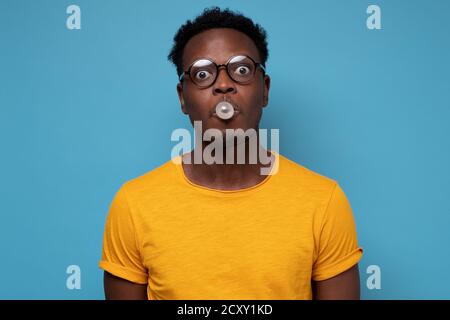 Young african american man in glasses inflating ball with chewing gum Stock Photo