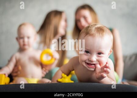 Two young girls play with their cute children in the apartment. Happy baby laughs Stock Photo
