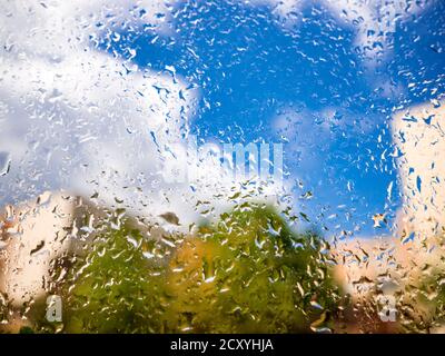 Rain drops on the window glass. Blurred background with house, greenery, clouds and blue sky Stock Photo