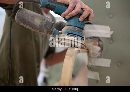 Close up view of someone power sanding the arm of an antique chair Stock Photo