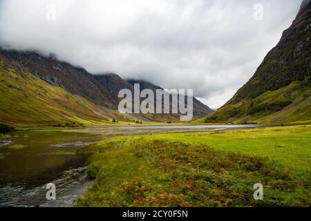 River and meadow vegetation with clouds covering the mountains Stock Photo