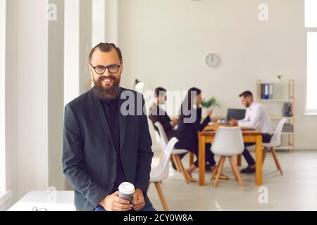 Happy young businessman with coffee to go in modern coworking space with busy people in background Stock Photo