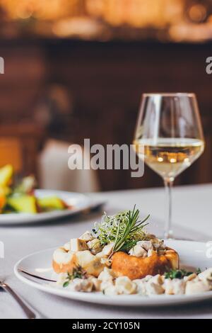 Stuffed mushrooms filled with cheese, mushroom stem and microgreen on the white plate with a glass of wine Stock Photo