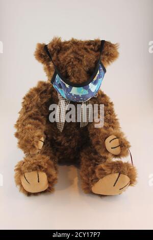 Brown teddy bear wearing a dinosaur kids face mask isolated on a white background with copy space Stock Photo