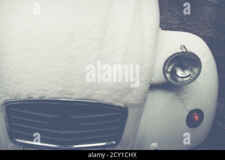 Vintage classic white bonnet of a old timer car snowed under with a typical grill and headlights Stock Photo