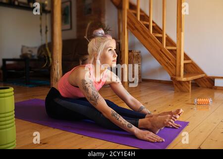 Young woman with a tattoo and foam roller aside. Fitness virtual online exercise. Stretching from the internet at home. A sporty girl in sportswear Stock Photo