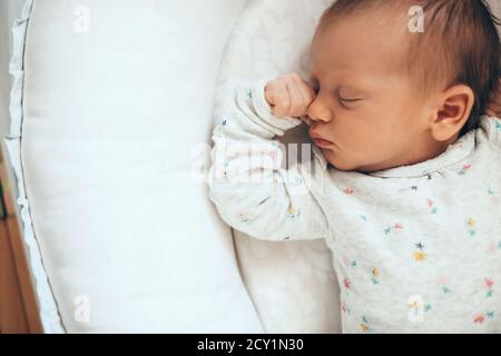Upper view photo of a newborn baby sleeping in safe on a white bed near some free space Stock Photo