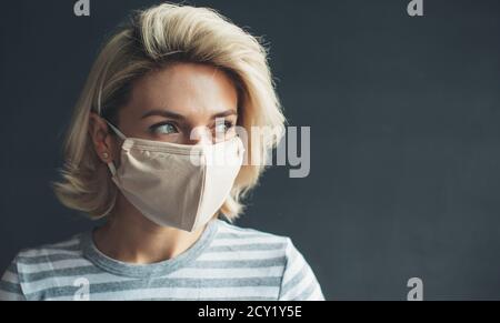 Close up photo of a blonde woman with mask on face looking at empty space near her advertising something on a dark gray studio wall Stock Photo