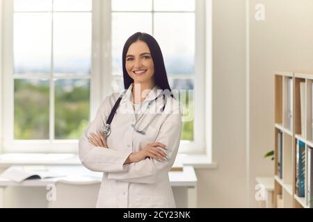 Young doctor standing arms crossed looking at camera and smiling in modern hospital office Stock Photo