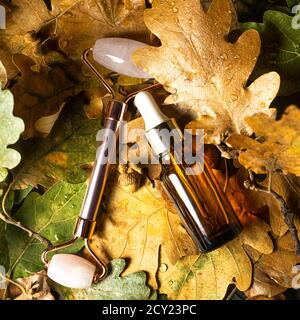 Autumn Beauty product creative composition. Beautiful autumn leaves and Rose quartz facial Jade roller with serum. Massaging tool for beautuful face and body. Flat lay, top view, copy space. Stock Photo