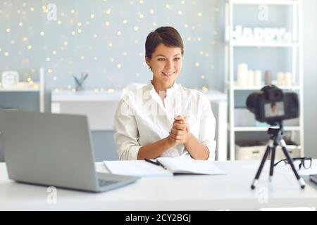Happy young female vlogger recording video for followers sitting at desk in cozy home office Stock Photo
