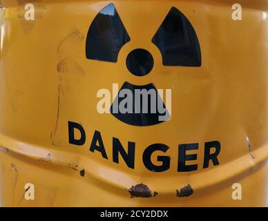 Black danger sign on yellow painted rusty metal barrel with rumpled damaged surface Stock Photo