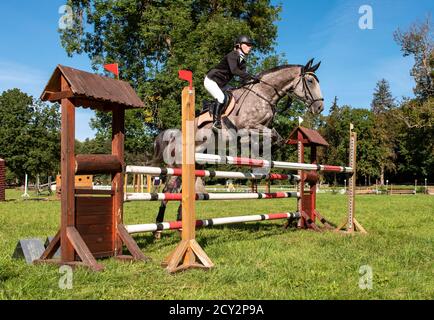 Low-angle view of young female rider and warmblood horse jumping over a fence at a showjumping eventing trial, Czech Republic Stock Photo