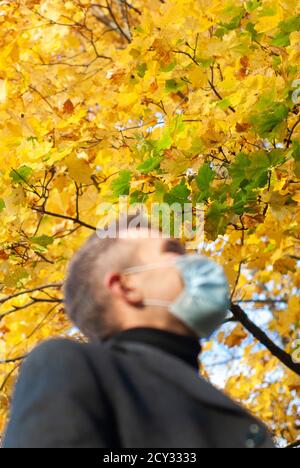 A man in a medical mask in an autumn Park, out of focus, close-up, Stock Photo