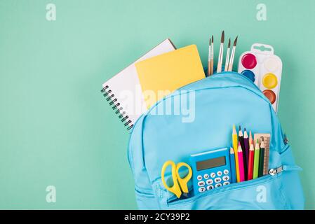Back to school concept. Top above overhead view photo of full blue backpack filled with school stationery isolated on turquoise background Stock Photo