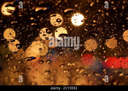 Closeup raindrops on the car windshield surface, with blurry urban street lights at night Stock Photo