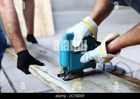 Two carpenters in working process in the carpentry workshop. Carpenter using fretsaw for cutting wooden boards. Construction details of male worker or Stock Photo