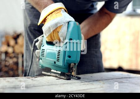 Carpenter using fretsaw for cutting wooden boards. Construction details of male worker or handy man with power tools.Work process in the carpentry Stock Photo