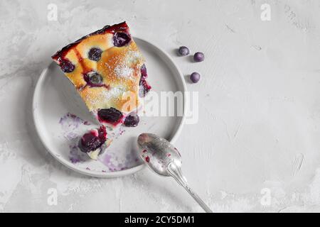 A slice of homemade clafoutis cherry pie - traditional french tart in a gray plate with a spoon on a gray background top view Stock Photo